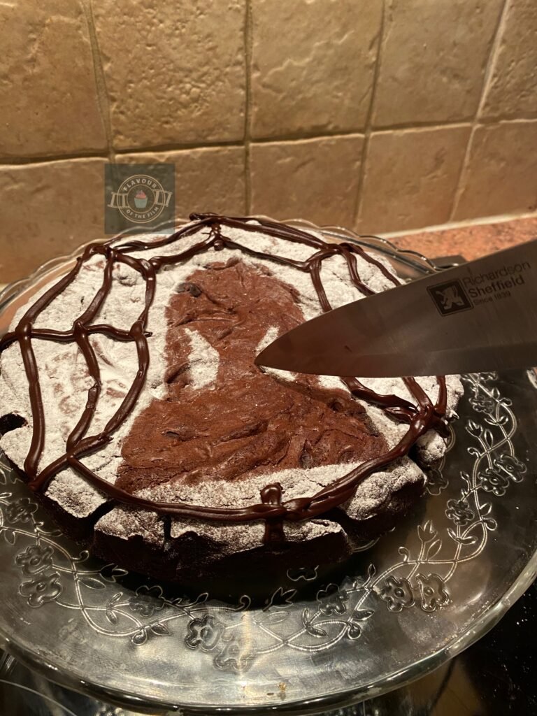 All images are of a round double chocolate brownie slab that is fully dusted with icing sugar, leaving a gap that is of Wednesday Addam's silhouette. The brownie slab is also decorated with dark chocolate ganache, piped to resemble a spider's web.