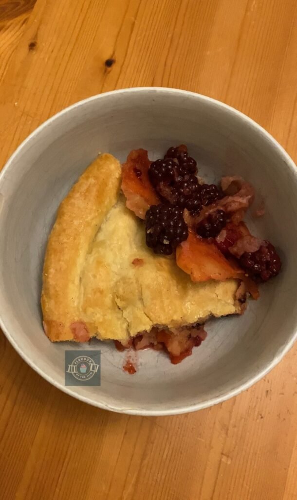The image is of a slice of the double crust apple and blackberry pie in a white serving bowl, with chunks of cooked apple and blackberries visible.