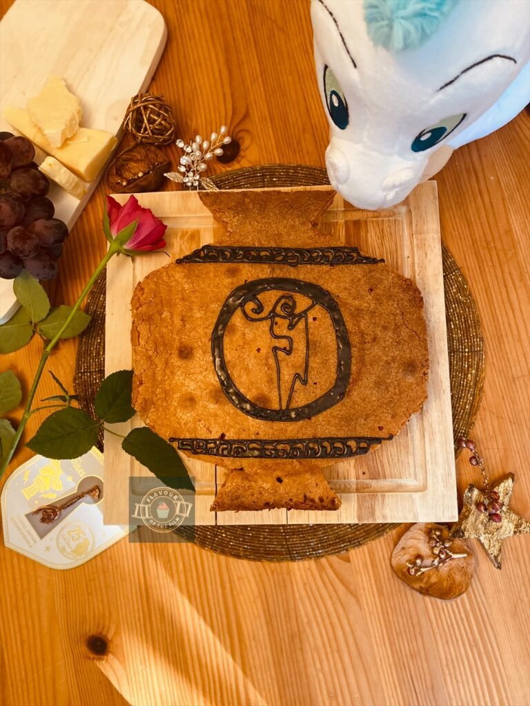 All images are of a Bakewell slice that is tinted orange and is shaped like an Ancient Greek vase. The design on the Bakewell is Hercules's lightning bolt medallion, piped in black royal icing. The Bakewell is presented on a wooden board. Props around it include a Pegasus plushie, 25th anniversary Disney Hercules key pin, a cheese board with cheese and grapes, a pink rose, and small gold knicknacks.
