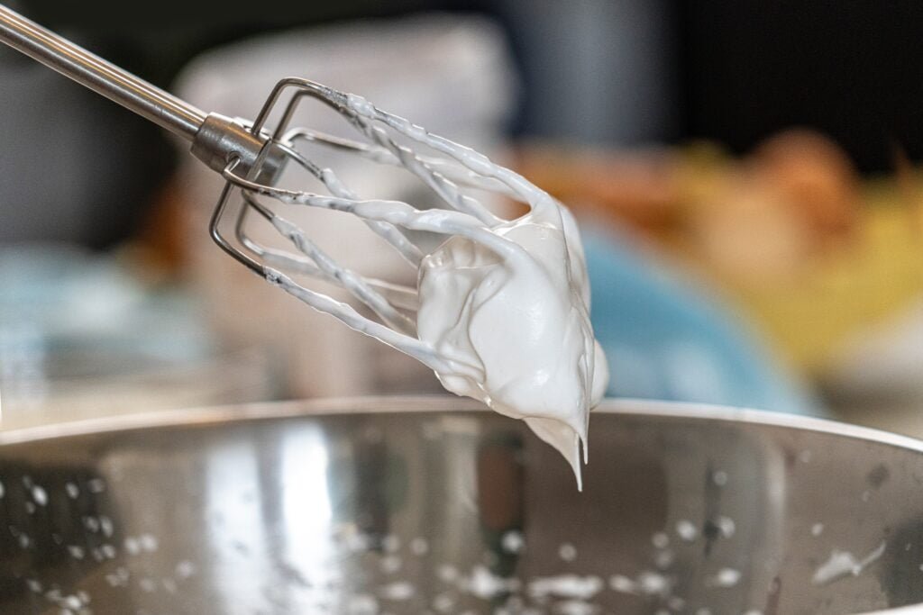A close up of a whisk covered in plain swiss meringue buttercream is hovering over a silver mixing bowl. This image goes with the introduction of my top 10 baking tips.