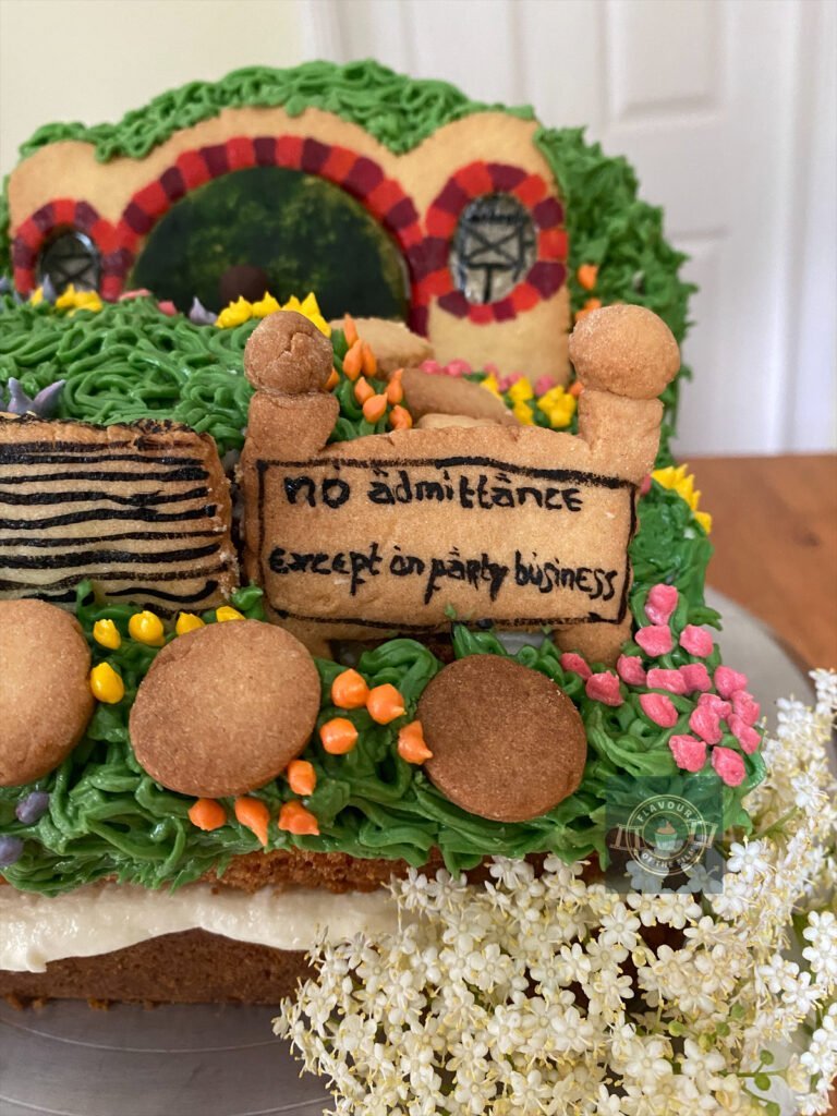 All images are of a square lemon and elderflower landscape cake that is decorated with buttercream, extra cake and biscuit decorations all in the shape and look of the hobbit hole known as Bag End, celebrating The Hobbit films. The cake is finished with the flowers from an elderflower tree.