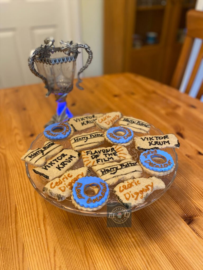 All images are of spiced biscuits shaped and decorated to resemble the pieces of paper than name the champions of the Tri Wizard tournament. The biscuits are all painted and hand decorated with icing pens to make them look personalised to each champion, and also charred from the flame of the goblet of fire. In the back of every image, there is a toy light up goblet of fire. These biscuits celebrate Harry Potter and the Goblet of Fire.