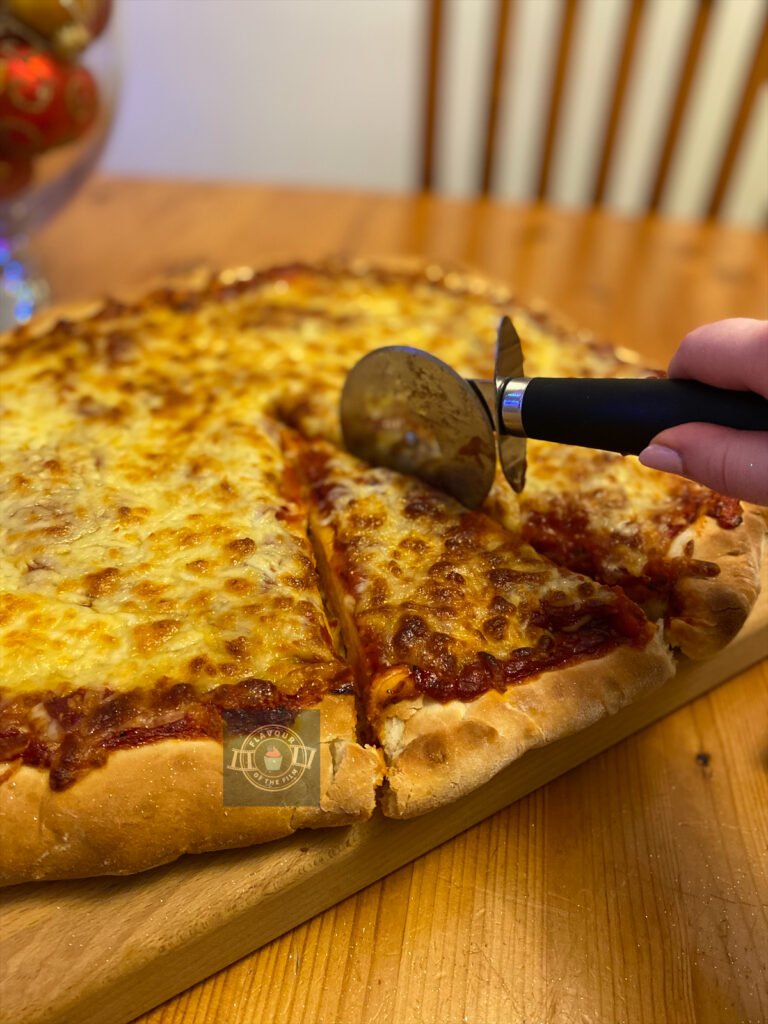 Thick Chicago style pizza being but with a pizza cutter. Cheese on the pizza is slightly glittery thanks to edible glitter which was added for a festive flare. This pizza celebrates Home Alone.