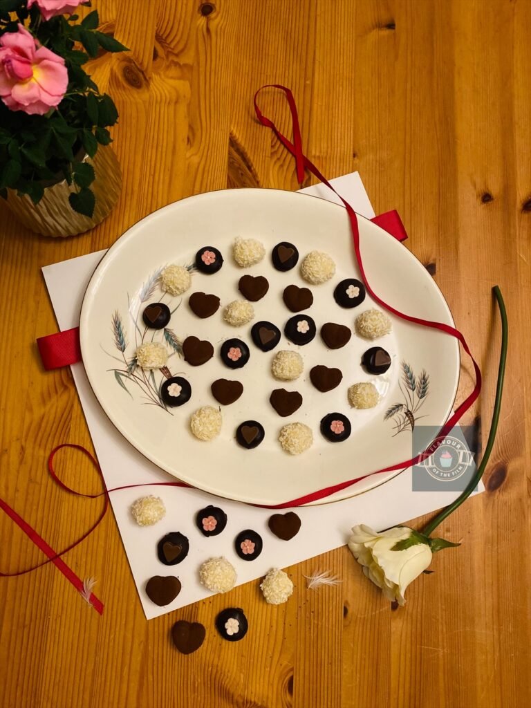 All images are of a collection of small chocolates. Some are white chocolate truffles covered in coconut shavings, some are fudge discs covered in dark chocolate and either topped with pink and white cherry blossom candy or chocolate hearts, and some are heart shaped truffles lightly dusted in cocoa powder. This life is like a box of chocolates selection celebrates Forrest Gump.