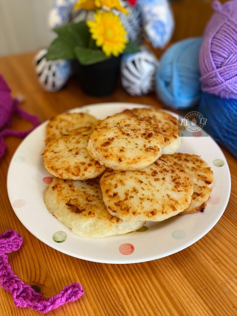 All images are of white cornmeal arepas con queso with a golden crispy exterior. The arepas are stacked on a multi-coloured polka dot white plate. Props around the arepas include brightly coloured balls of yarn in fuschia, lilac, light blue and dark blue, as well as a pot of yellow flowers and a teddy bear made of various colourful materials.