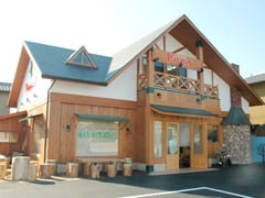 Fairytale style building (Peter Pan Suruga Kitchen, Shizuoka) with mostly wooden exterior and some exposed stone work. Log seating and tables are arranged around the front, near the double door entrance.