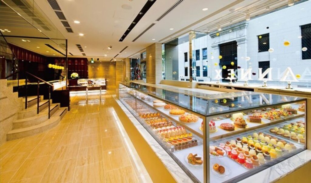 Bakeries in Japan: inside of Wako Cake and Chocolate Shop, Ginza, Tokyo. Wooden interior with large front glass windows and cake display cases showcasing rows of patisserie style treats.