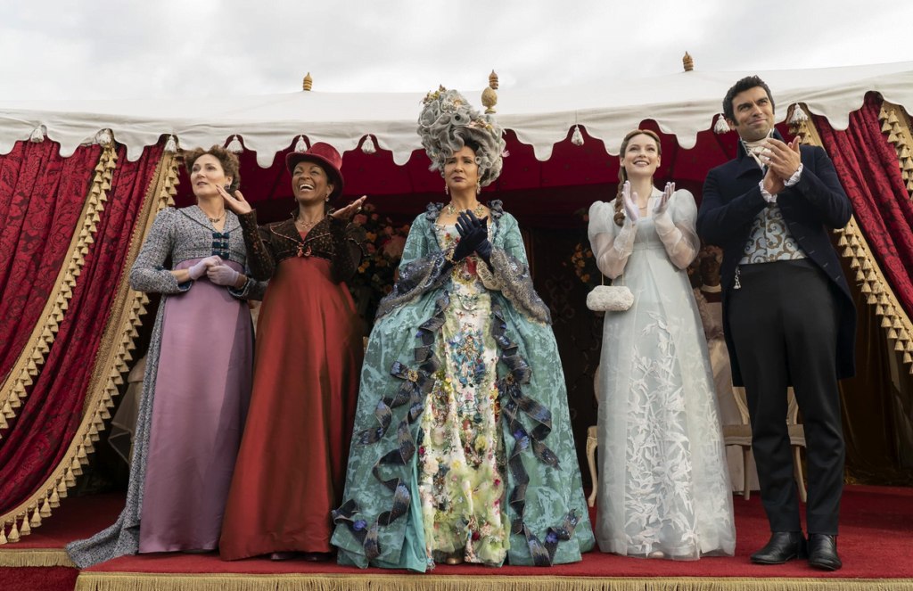 Queen Charlotte clapping, with Lady Bridgerton, Lady Danbury, Francesca Bridgerton with a suitor on either side of the Queen.