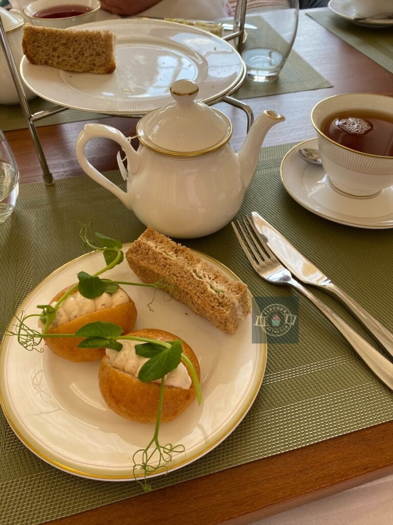 Four finger sandwiches on a cream plate: two salmon mousse rolls and one cream cheese and two cucumber and cream cheese on wholemeal bread.