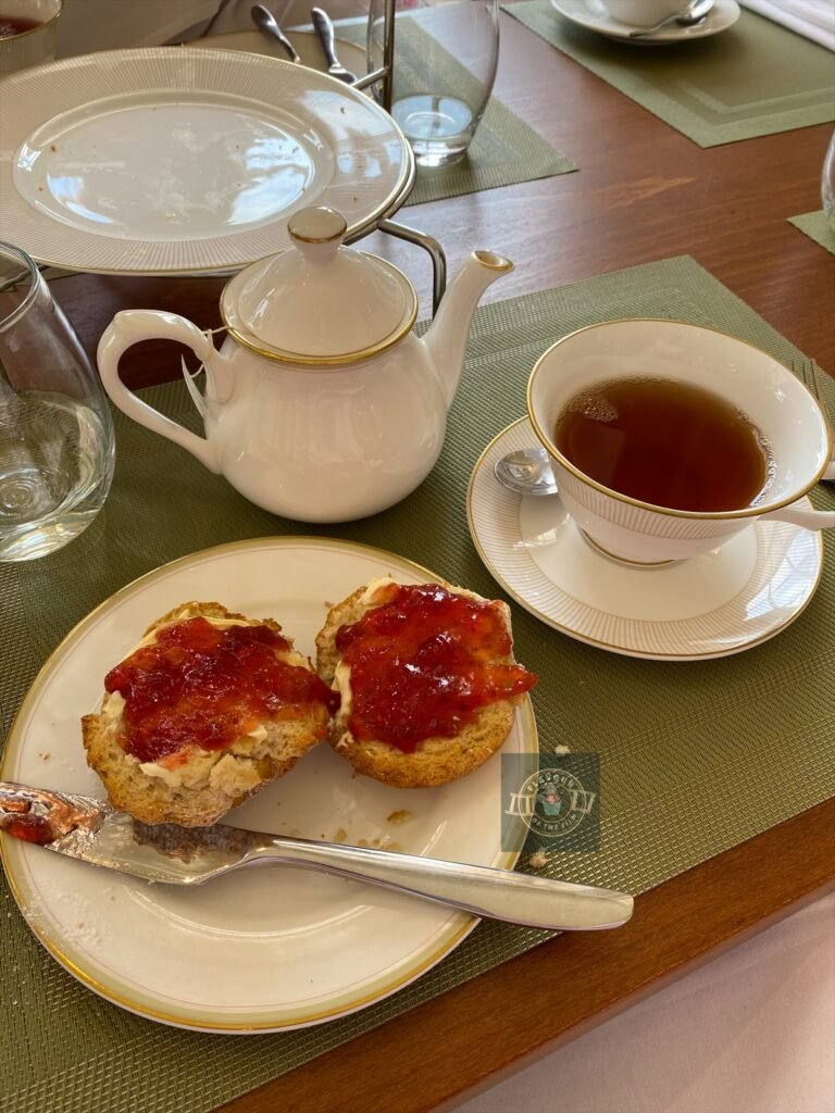 Fruit scones with clotted cream and jam beside a pot and cup of Earl Grey tea.