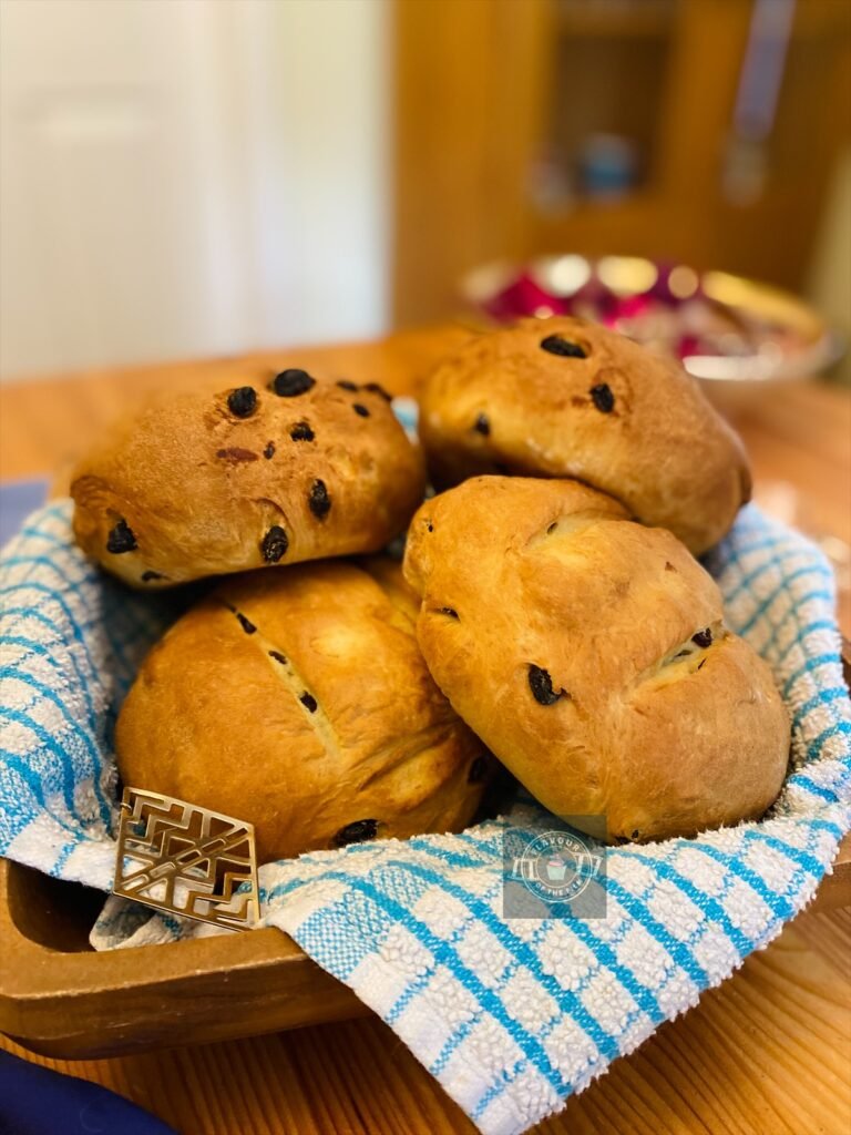 All images are of four golden loaves of bread that are white on the inside and are filled with raisins. The loaves are displayed on a wooden square dish with a blue and white checked tea towel. Props include Aztec gold earrings, a scouts neckerchief, and red and gold natural pieces displayed in a gold dish.