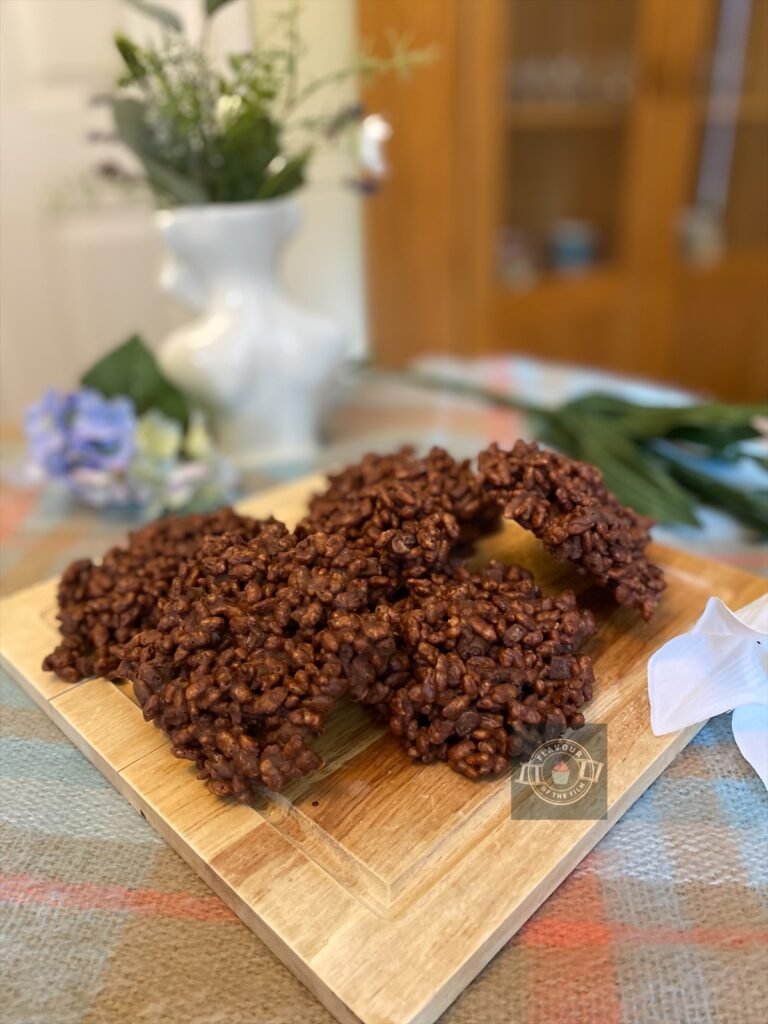 Chocolate rice krispie treats shaped like hamburger patties, displayed on a wooden board with wildflowers around.