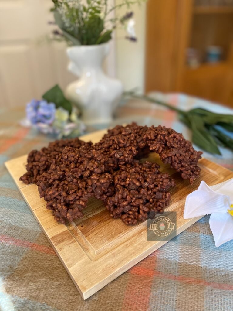 Chocolate rice krispie treats shaped like hamburger patties, displayed on a wooden board with wildflowers around.