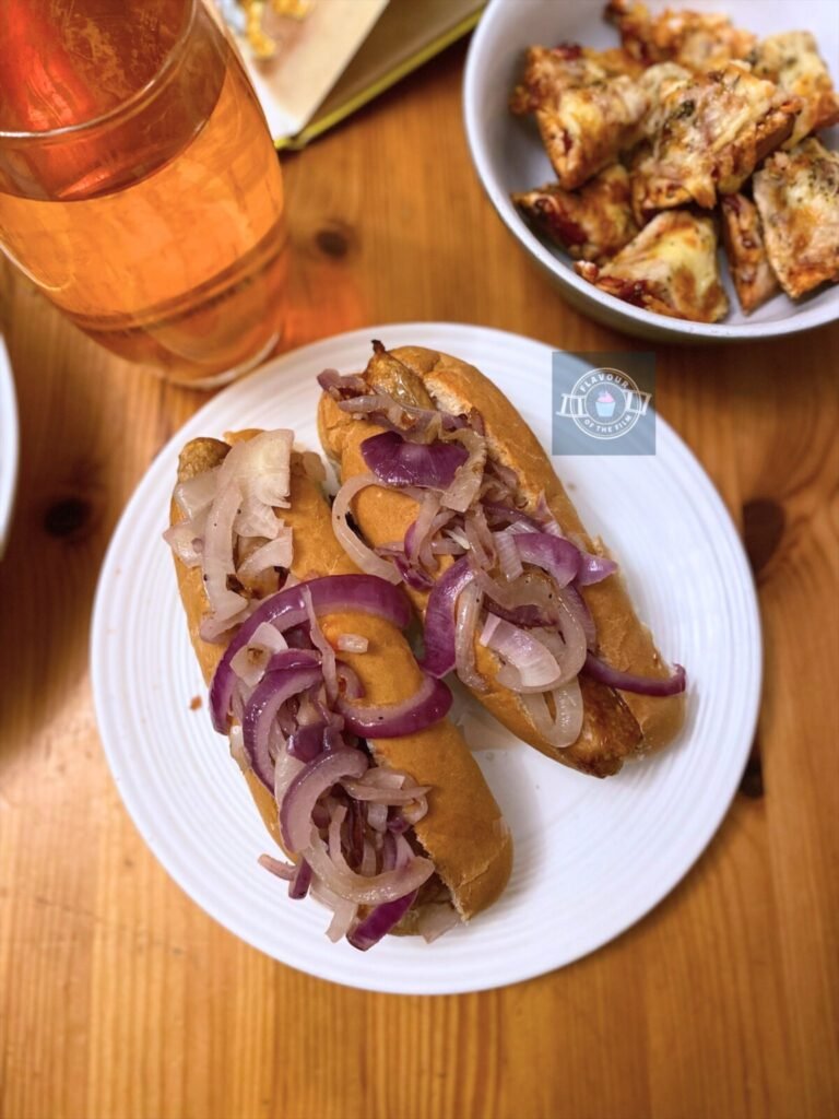 Two hot dogs topped with fried onions and ketchup plated next to the pizza bagel pieces and the glass of iced tea.