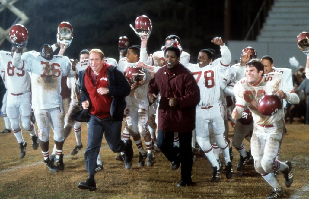 United football team running in celebration, led by the team coaches.