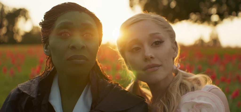 Elphaba and Glinda standing side by side with the sun setting behind them.