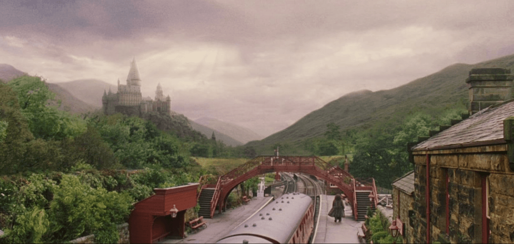 Hagrid walking in the distance with Hogwarts in the back as the train pulls away from Hogsmeade Station in Harry Potter and the Philosopher's Stone.