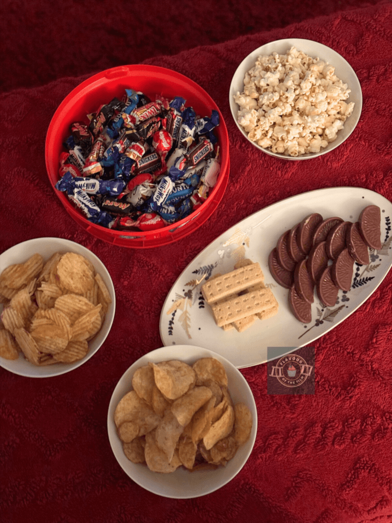 Birds eye view of two bowls of crisps, a tub of Celebrations chocolates and a festive plate of Scottish shortbread a Terry's chocolate orange slices.