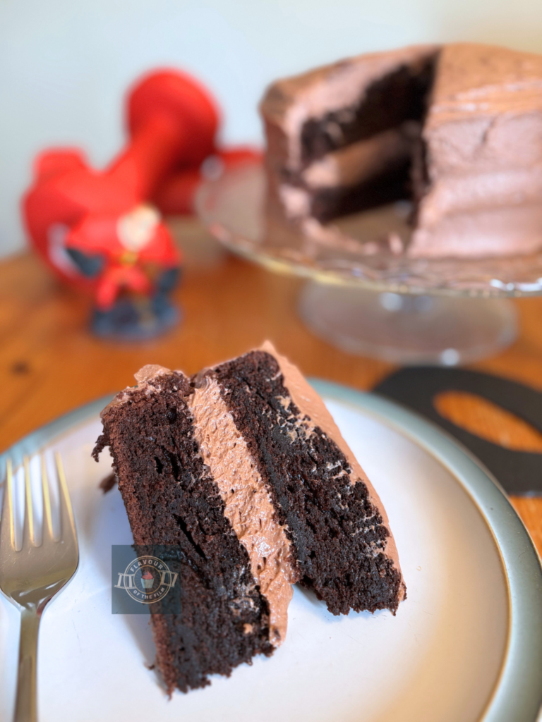 All images are of a two layer chocolate cake with light chocolate frosting. Most images are of a cake slice with the rest of the cake in the background. Props include a black card mask, red dumbbell weights and a gaming figure of Mr. Incredible.