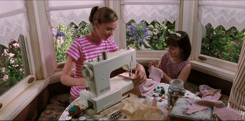 Matilda and Miss Honey sewing with the garden blooming as can be seen through the windows behind them.