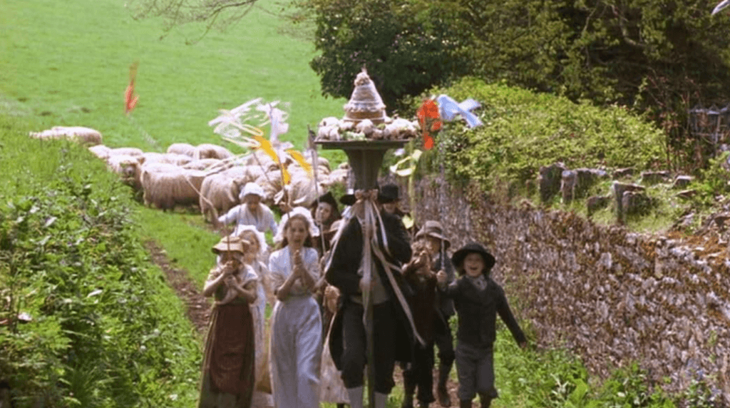 A rustic wedding cake being carried to the church by a man and a group of kids.