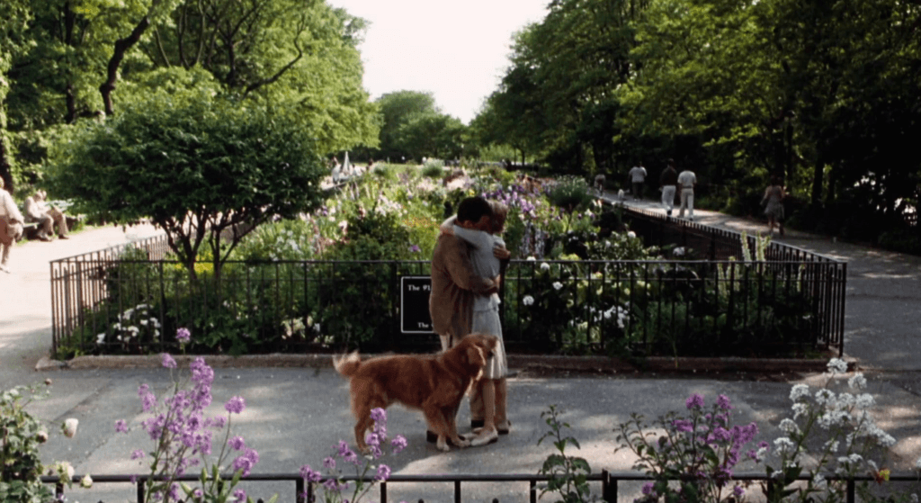 The two leading characters embracing in a blooming New York garden, with the gorgeous dog getting ready to join in.