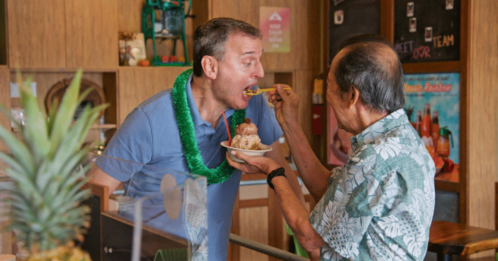 Phil being fed shave ice by the owner of the food place he's in.