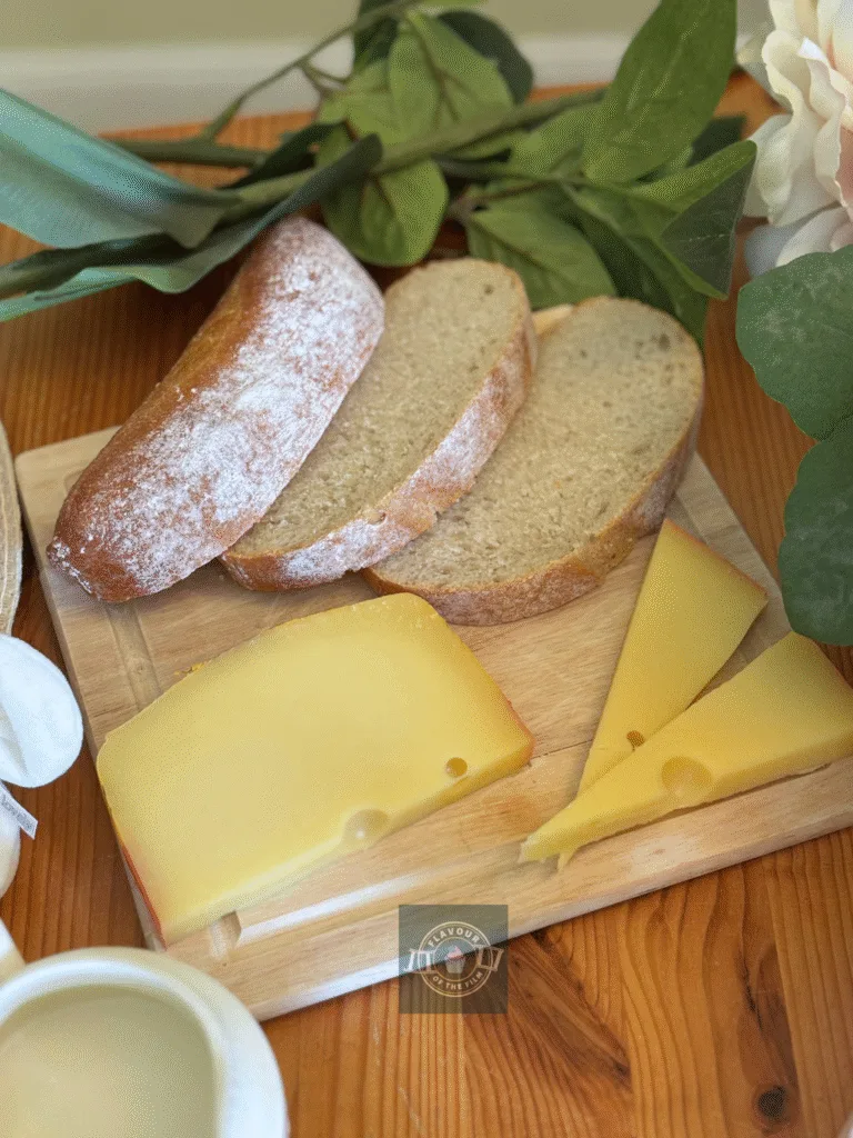 Bread and hard cheese both sliced and presented on a wooden board with flowers around it.