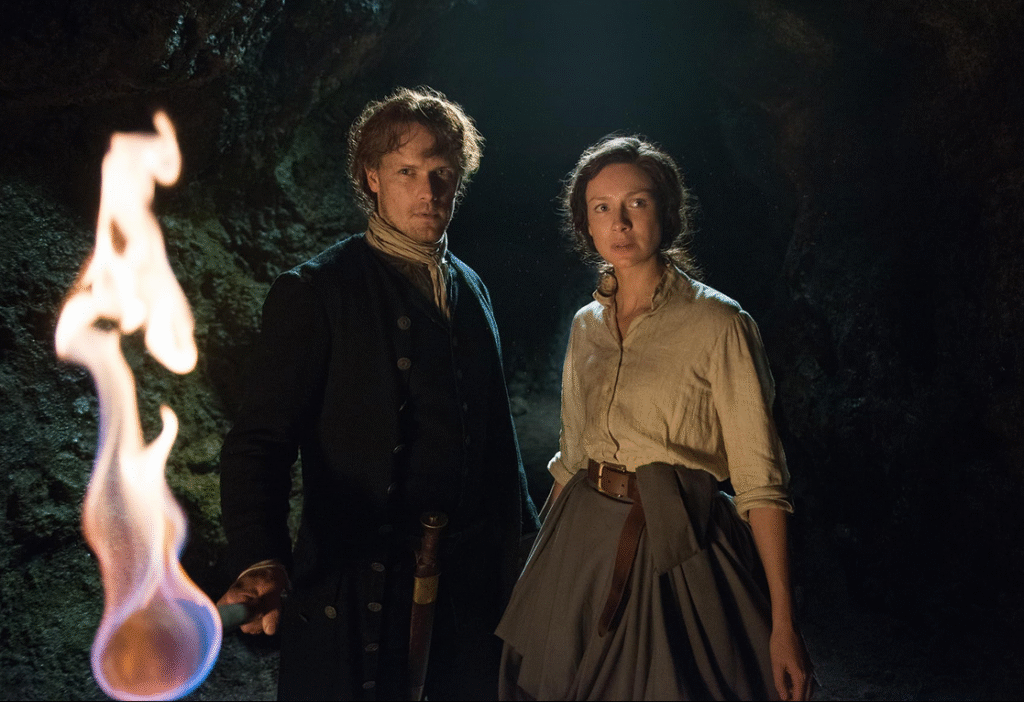 Jamie and Claire in the dark with a lit torch.
