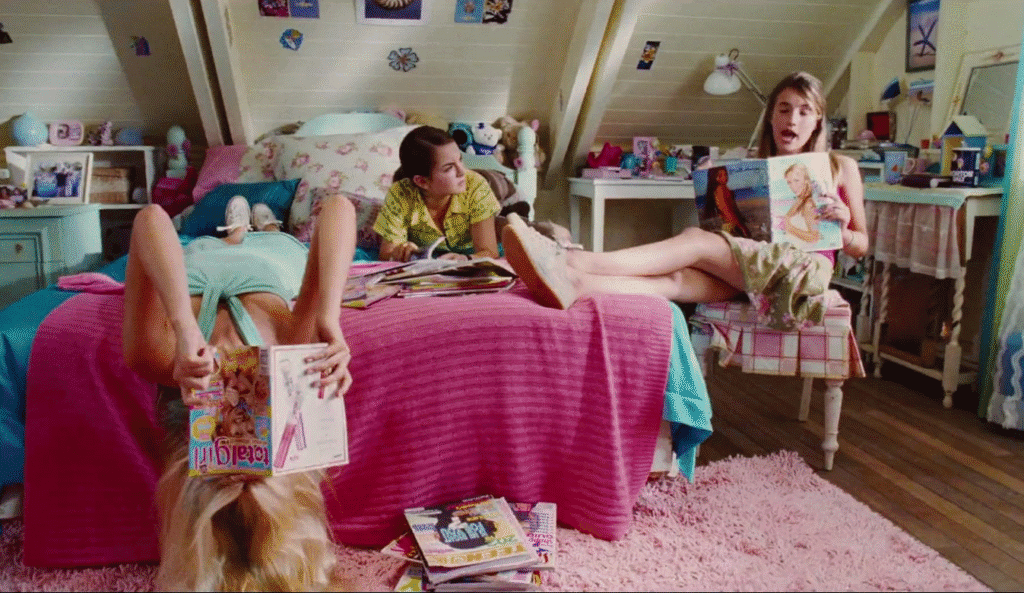 The three lead characters in a bedroom reading magazines.