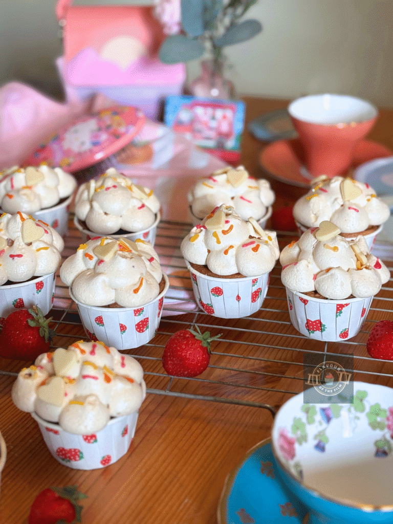 All images are of My Melody & Kuromi cupcakes in strawberry cupcake cases, topped with meringue clouds, white chocolate hearts, and sprinkles. Teh cupcakes are served on a wire rack. Props include pink oven gloves with peaches on, a Cinnamonroll fan, sunset bag, pink flowers in a pink vase, coral pink teacup and blue teacup, a Hello Kitty hairbrush, fresh strawberries, and a My Melody Amiibo card for Animal Crossing.