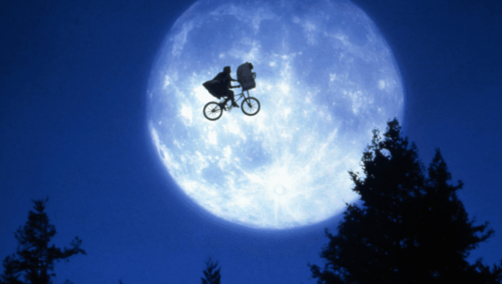 Elliott and E.T. cycling through the air in front of the moon.