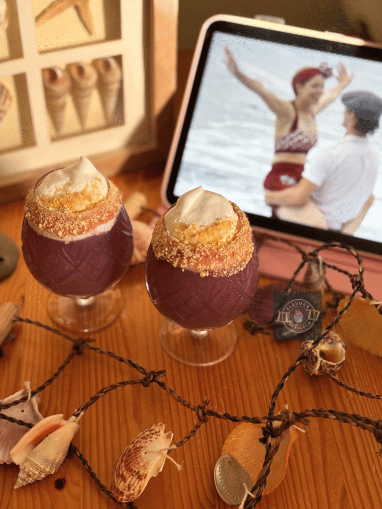 All images are of The Notebook movie night menu drinks which are a deep rouge with a golden biscuit crumb around the rim and a white meringue floating top. Props include the "I'm a bird" scene still on a tablet; a collection of seashells, a sea bird statue, and framed sea shells.