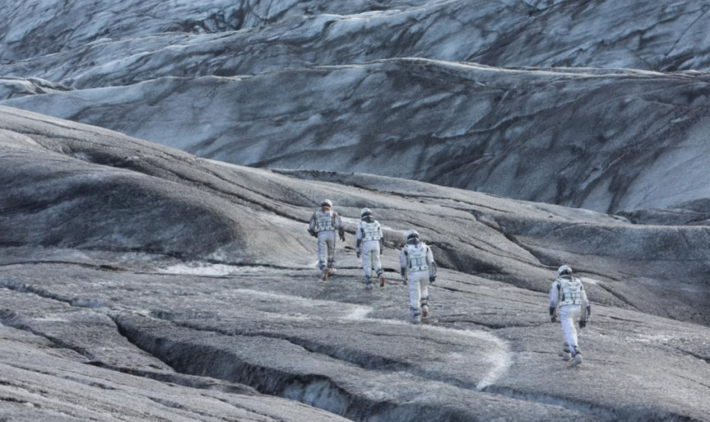 The crew walking across a grey terrain.