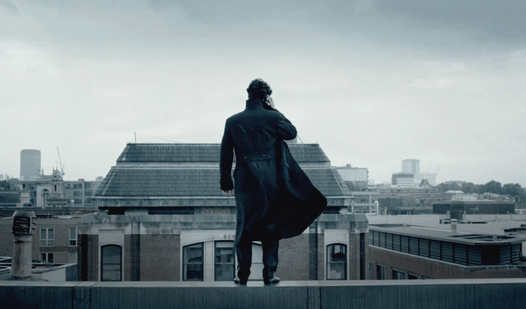 Sherlock standing on the ledge of a building.