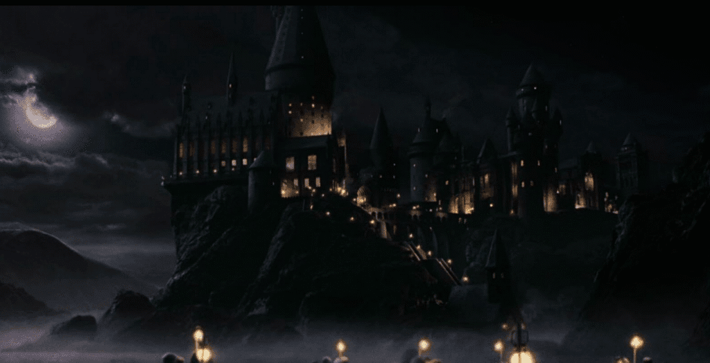 Hogwarts at night with only the window lights and the boat lanterns to light the way.